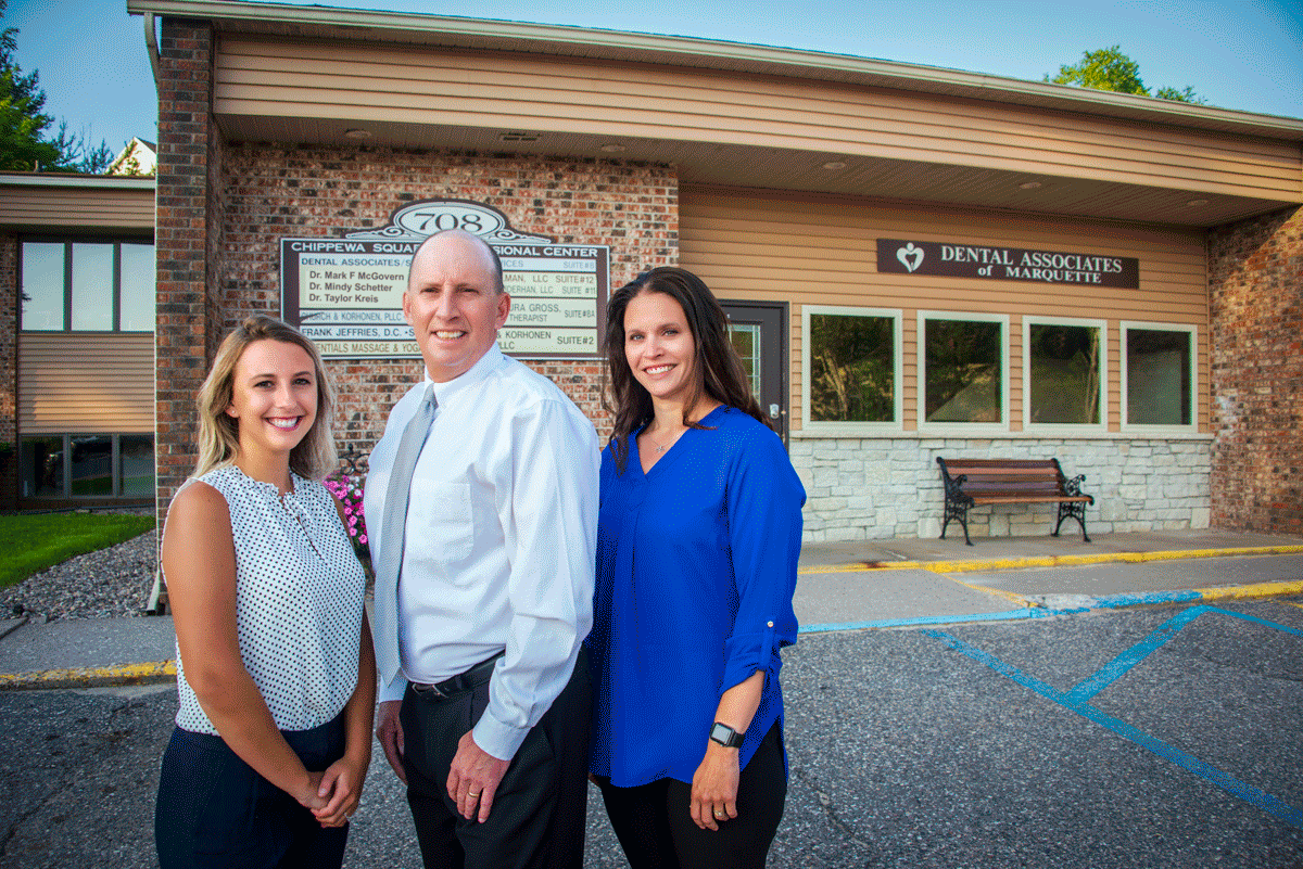 Three staff members outside the Chippewa Square Professional Center beside the Dental Associates of Marquette building sign